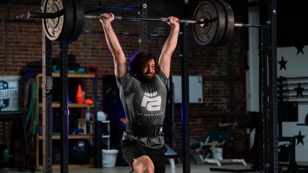 Woman squatting with a barbell wearing Fit Active Sports grey lever belt in a gym