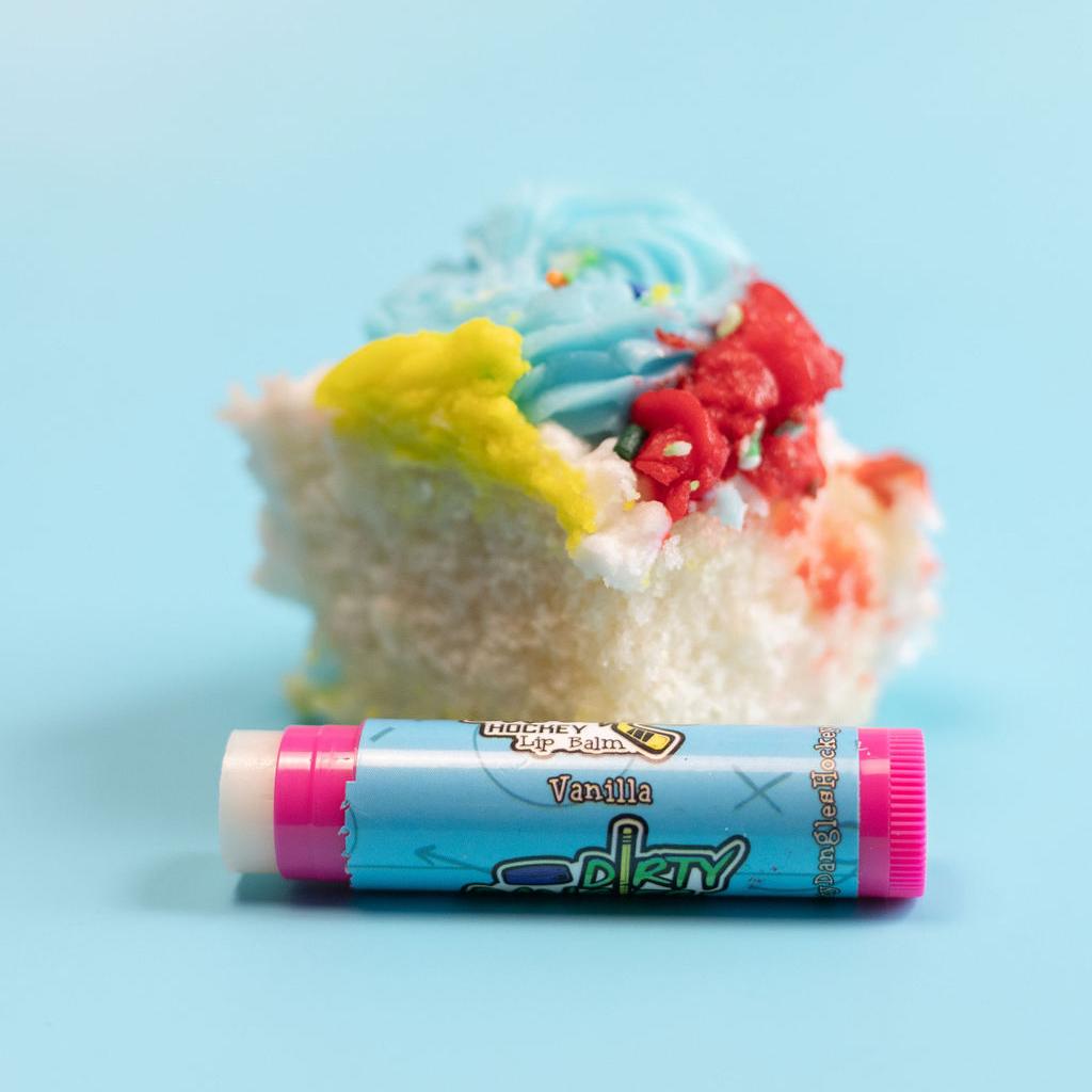 A pink stick of dirty dangles natural lip balm. Vanilla scent on a blue background with a piece of vanilla cake.