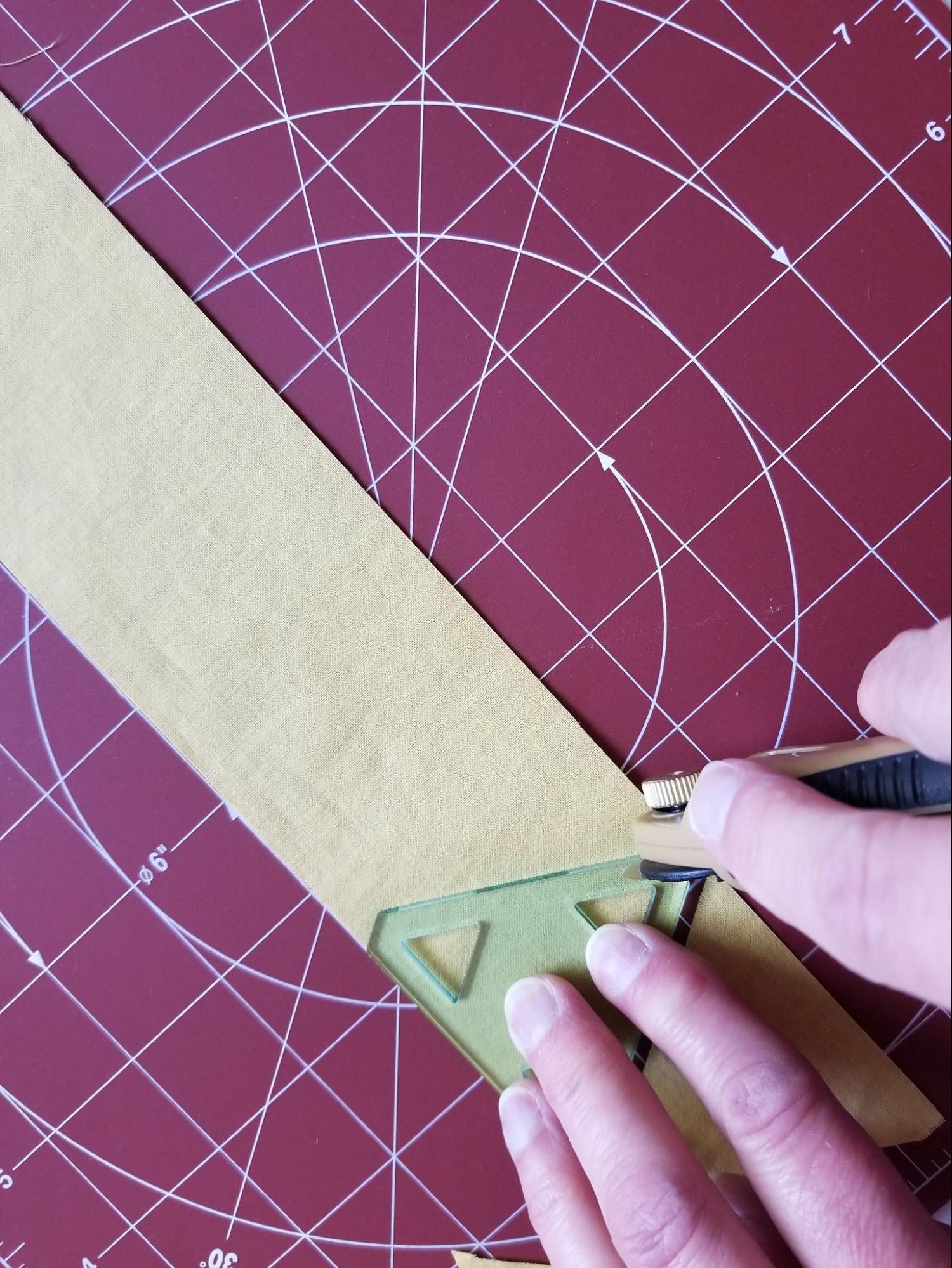 Cutting second triangle from a fabric strip using a 60 degree triangle quilt template.