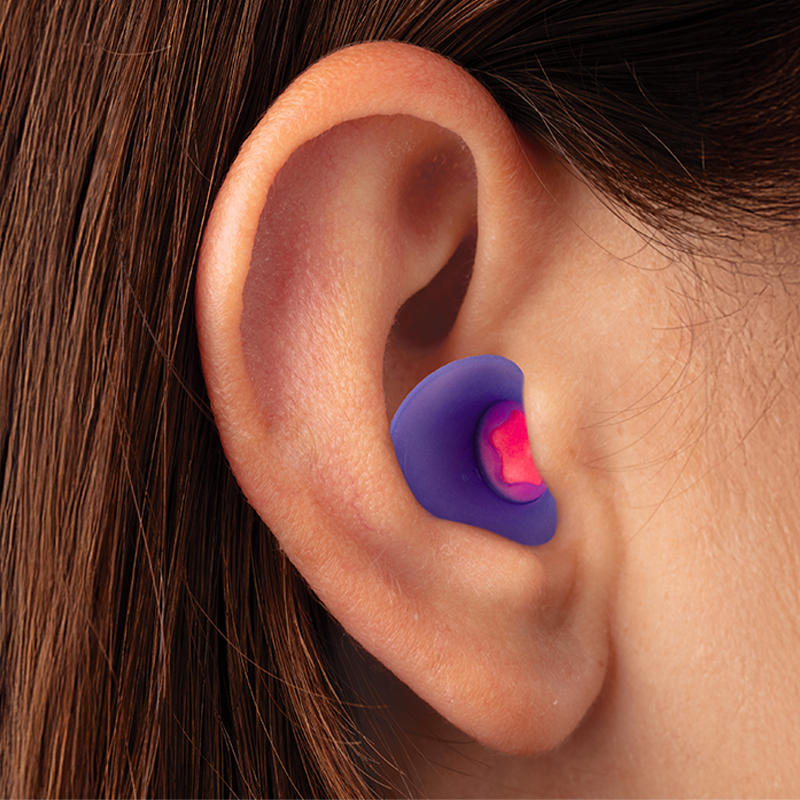 An image of a person’s ear with a purple and pink silicone and foam earplug seated correctly in their ear canal.