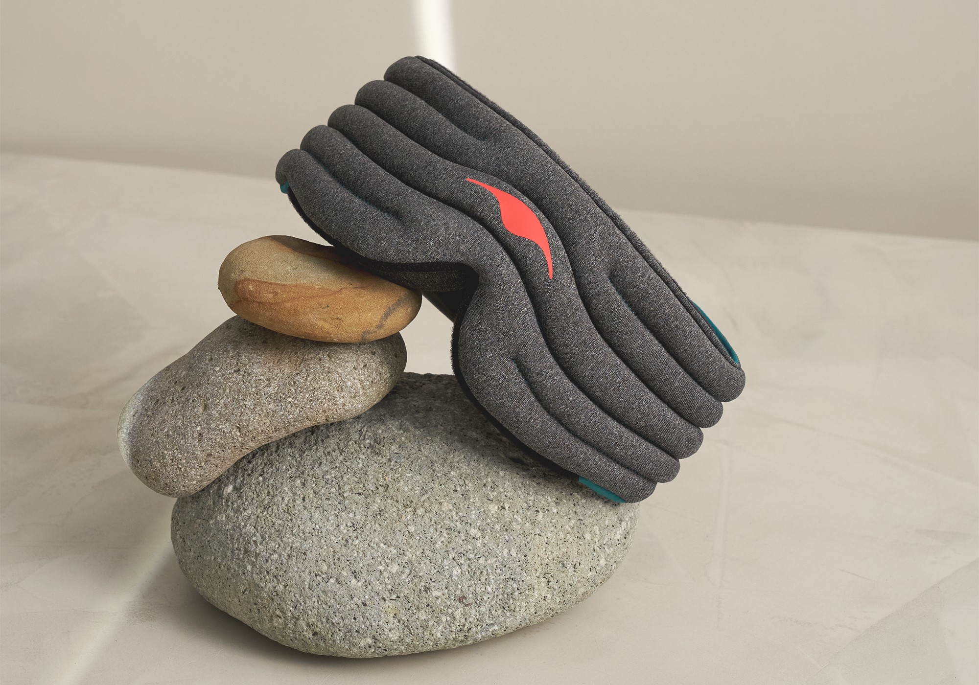 A gray weighted sleep mask resting on 3 pebbles of different sizes.
