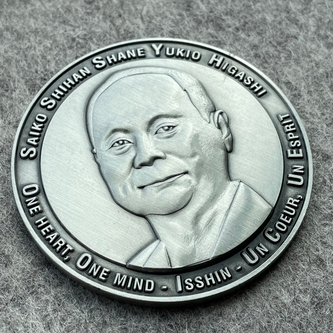a custommade silver metal sports coin with a potrait of carate school founder and logo ingraved along the edges