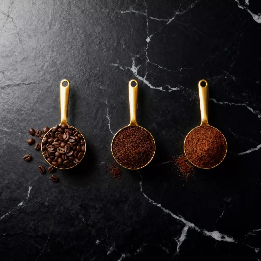 Three golden scoops showing whole bean, coarse ground, and drip ground coffee on a black marble surface.