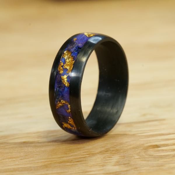The Fleur De Lis Ring has a carbon fiber band and features an inlay of various materials making for one unique black ring