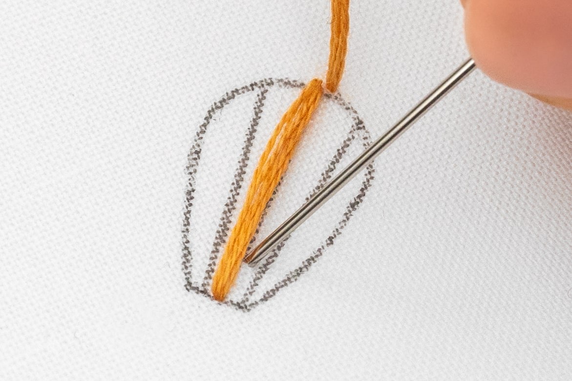 A needle pokes down next to the first bit of satin stitch.