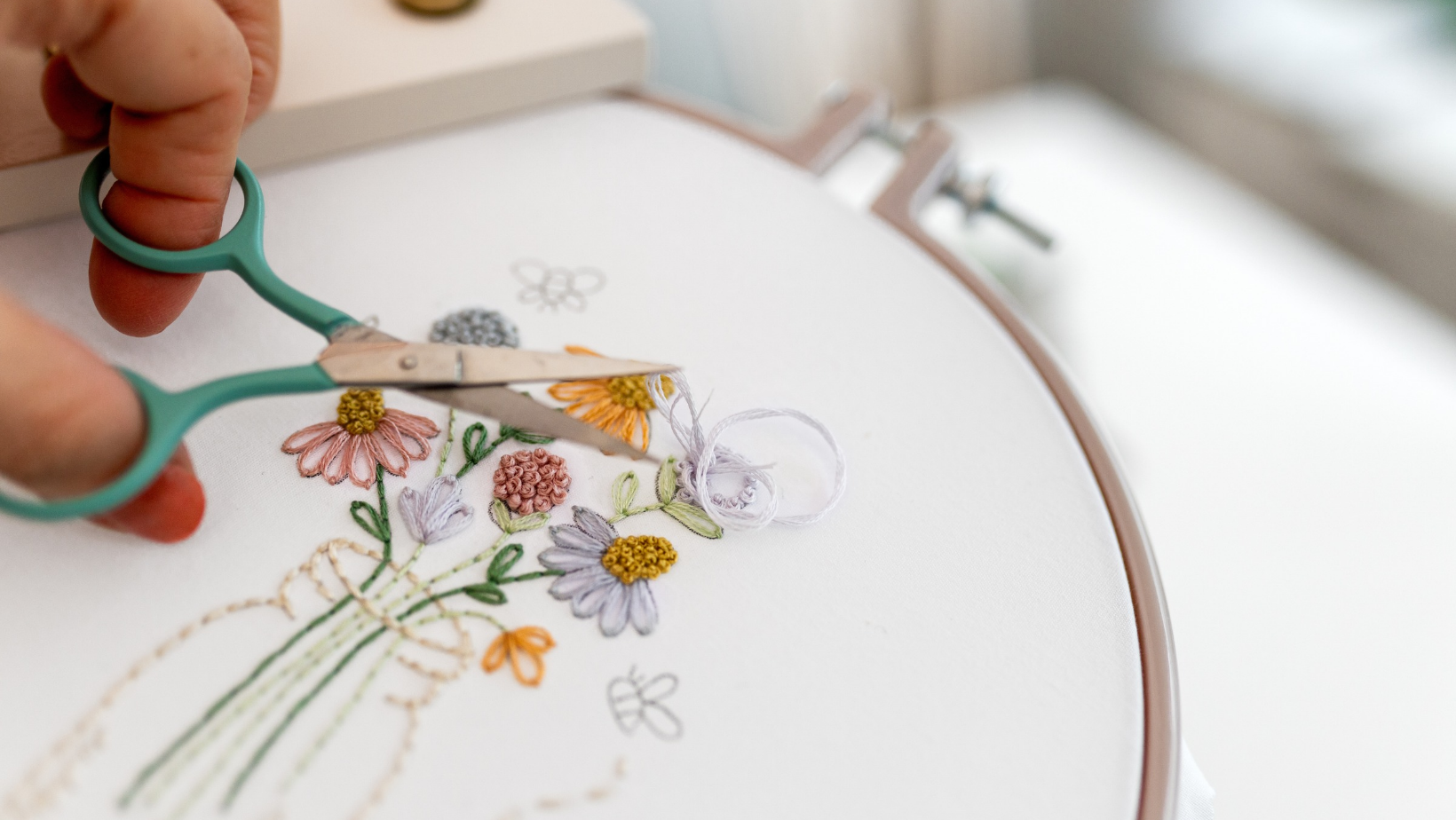 Green embroidery scissors snipping a thread tail on a partly finished wildflower bouquet design.