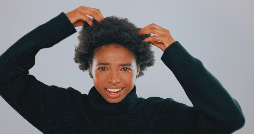 Black woman wearing an afro and her hands on her scalp