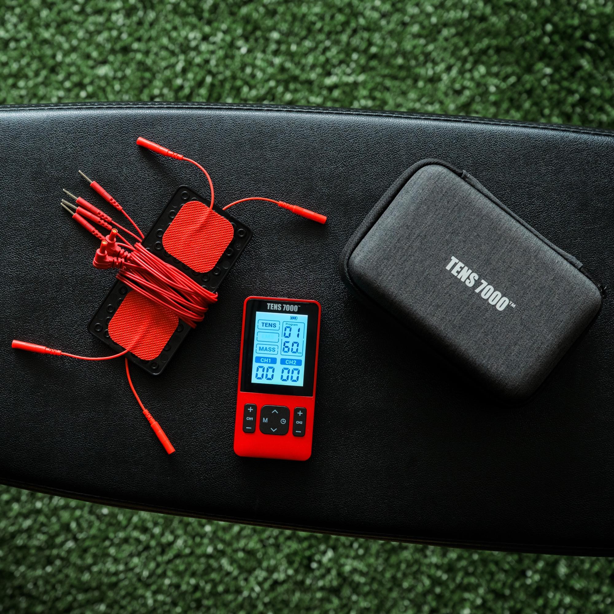 The TENS 7000 Sports TENS unit on a padded bench next to its electrodes and carrying case