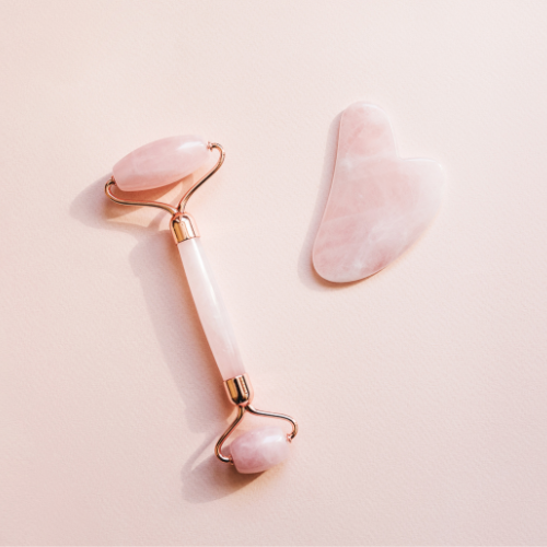 a pink jade roller and a pink gua sha tool on a light pink backgroudn.