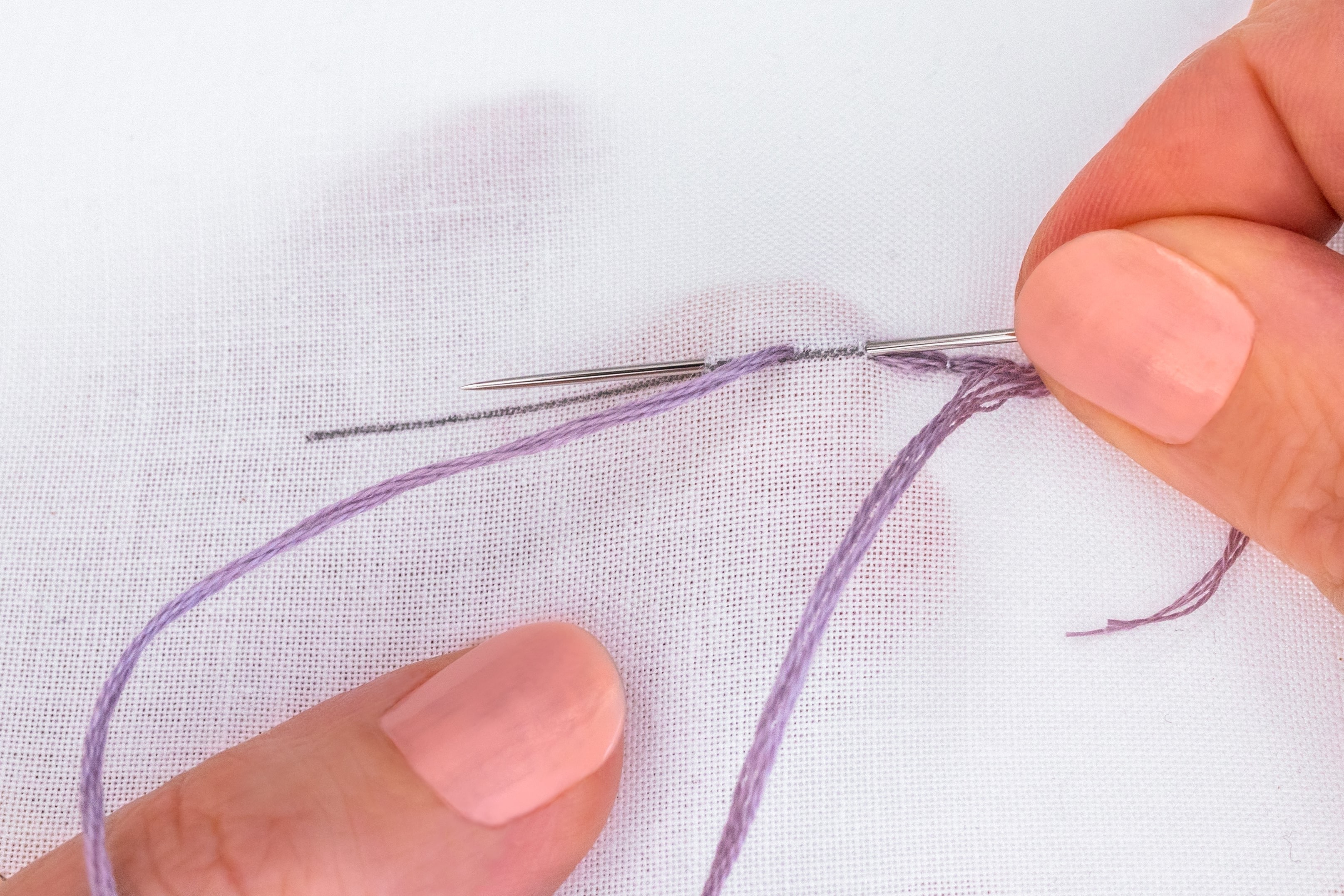 A hand sews a stitch in a line, creating a loop.