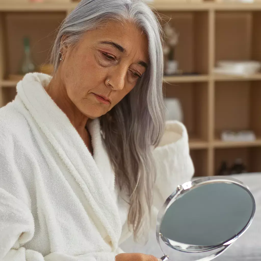 Woman looking in the mirror focusing on her puffy eyes