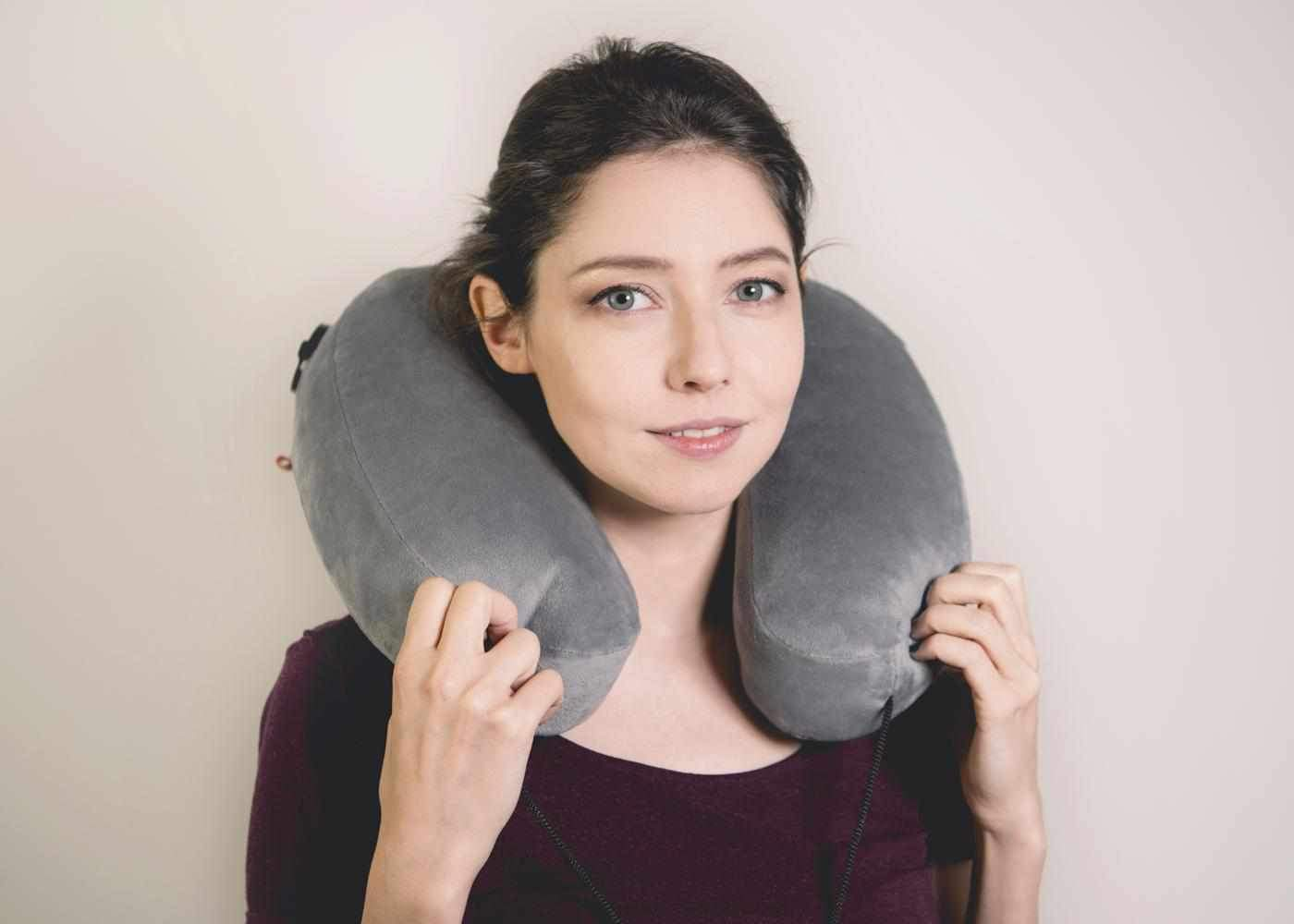 A brunette holding the tips of a travel nap pillow that’s around her neck.