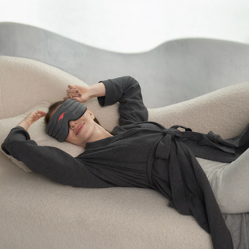 A girl in a robe reclining on a couch wearing the best weighted sleep mask for side sleepers.