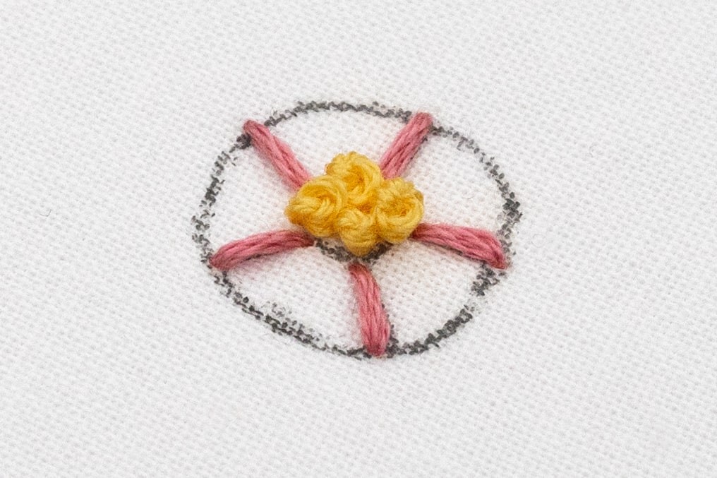 French Knots are clustered in the middle of the Woven Rose with spokes around.