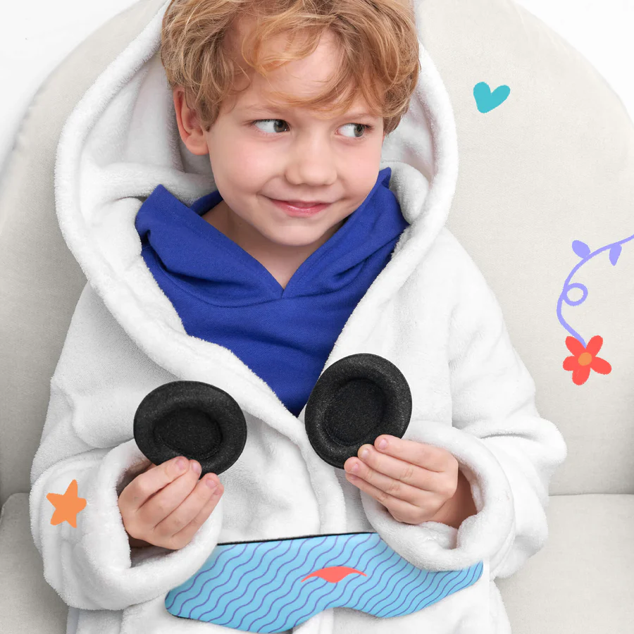 A kid wearing a white hoodie holding black eye cups for a sleep mask with kids. The blue head strap is on his lap.