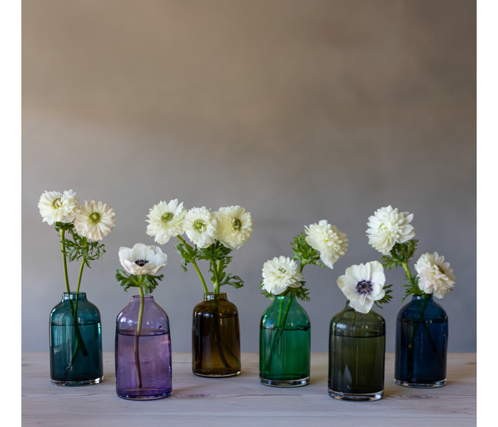 Glassybaby bloomettes transparent glass vases in various colors with flowers on a gray background