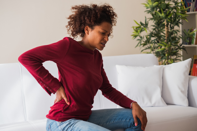 Woman clutching lower back in pain sitting on her couch