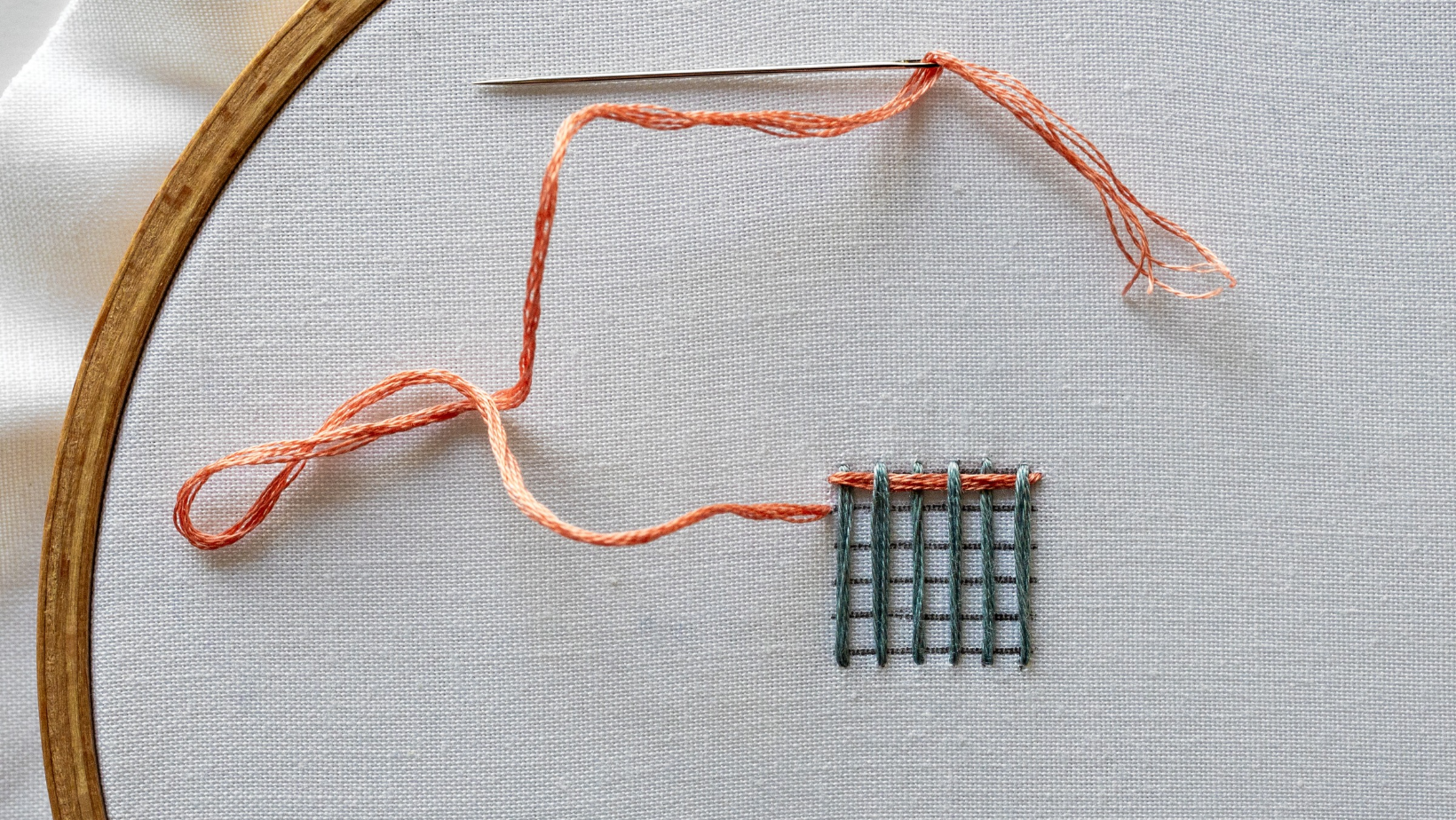 A needle going down into the fabric at the end of the first woven row.