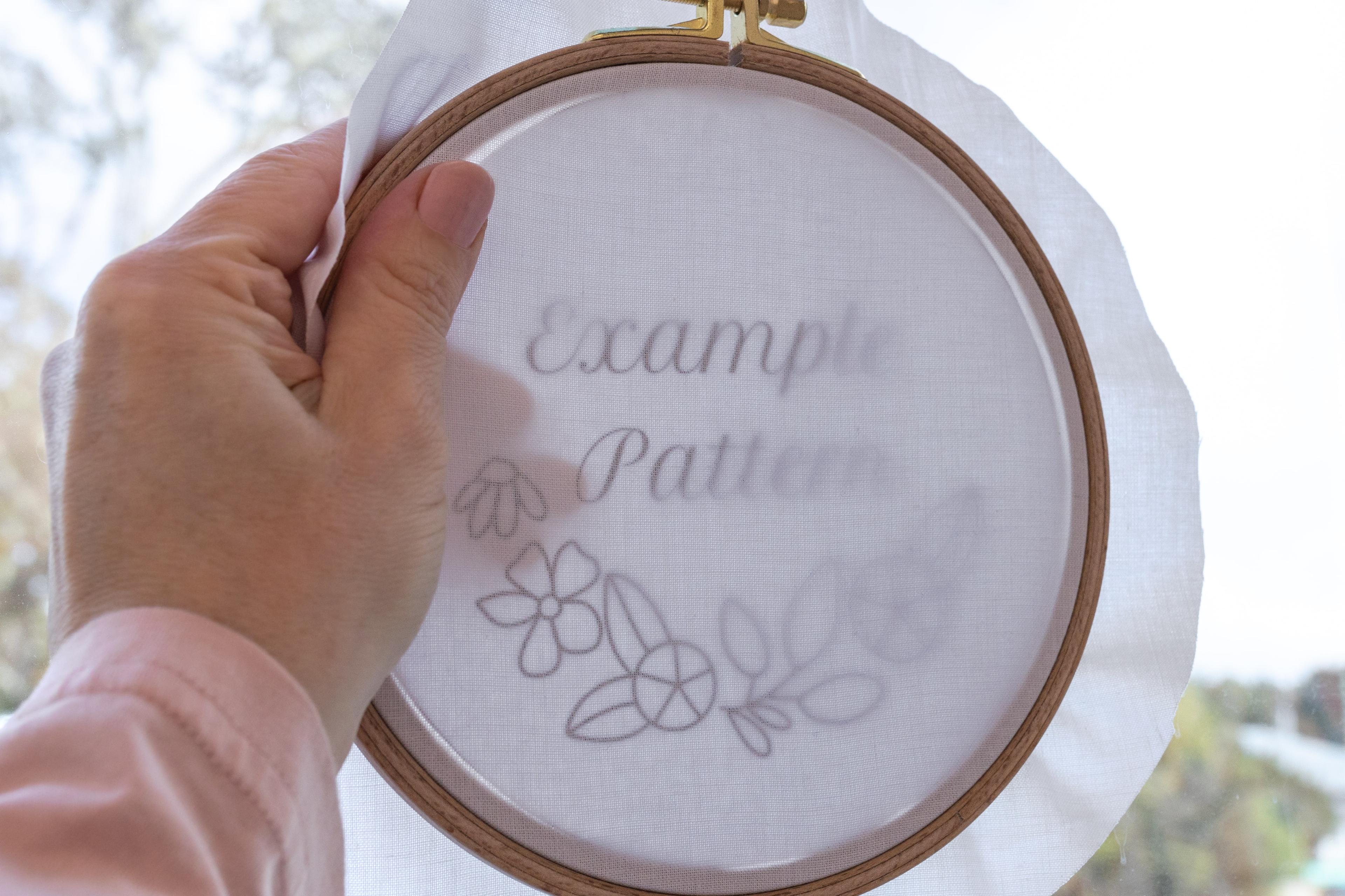 A hand holds a hoop with the pattern in front of a window.