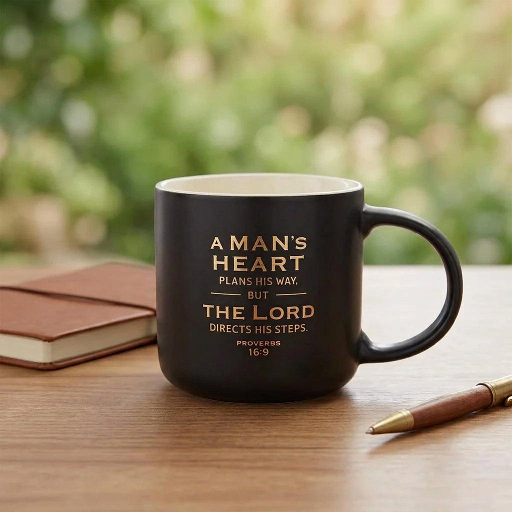 A Man's Heart black ceramic mug on a wooden table beside a Bible and pen