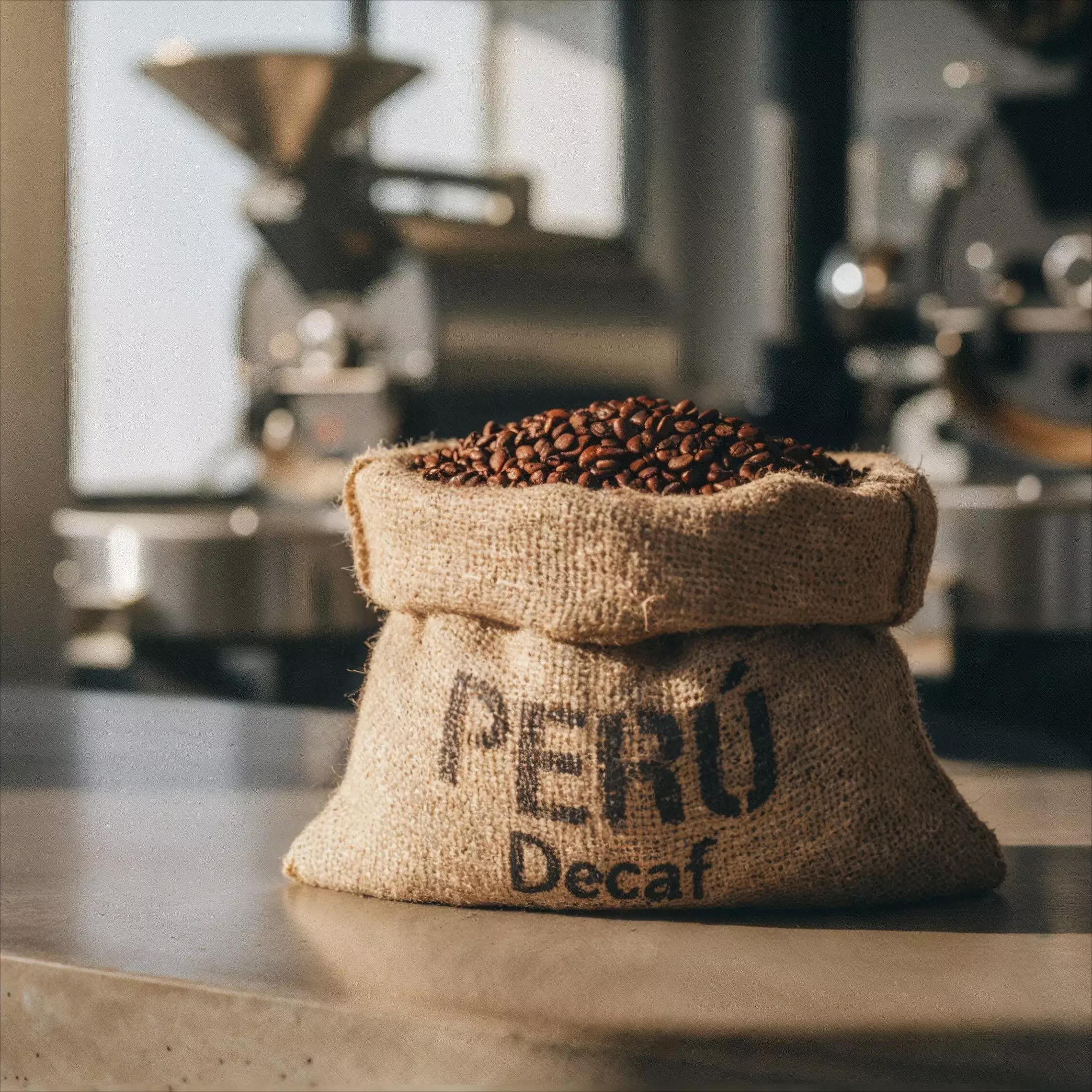 Bag labeled Peru Decaf filled with roasted coffee beans in a roastery setting for the Decaf Coffee category.