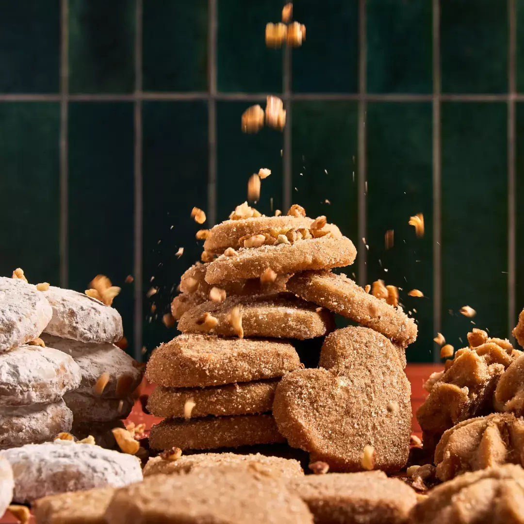 close up pile of small cookies with pecans sprinkled on them