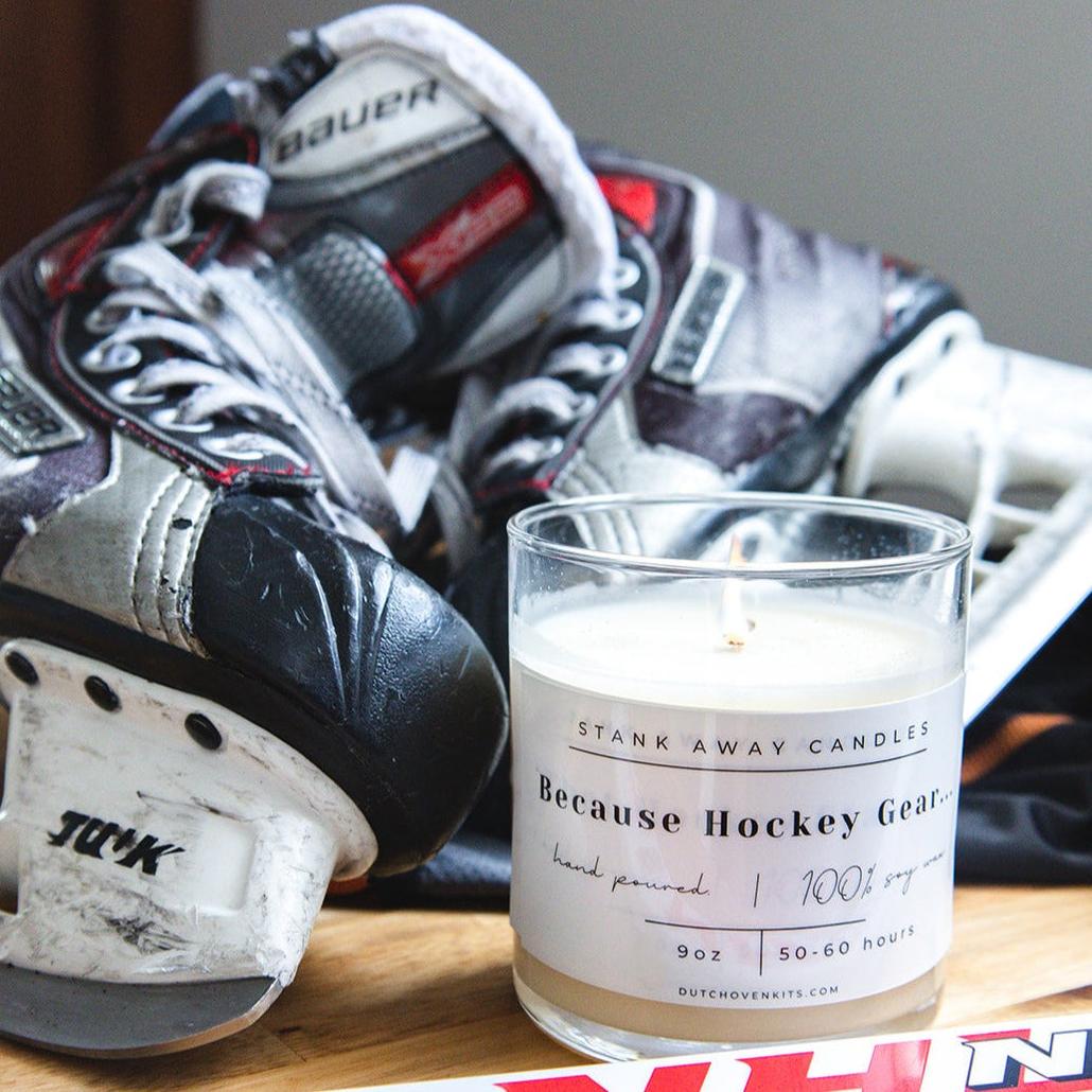 A white candle sits on a table with a pair of ice skates and a hockey stick. Because Hockey Gear Natural Soy Wax Candle