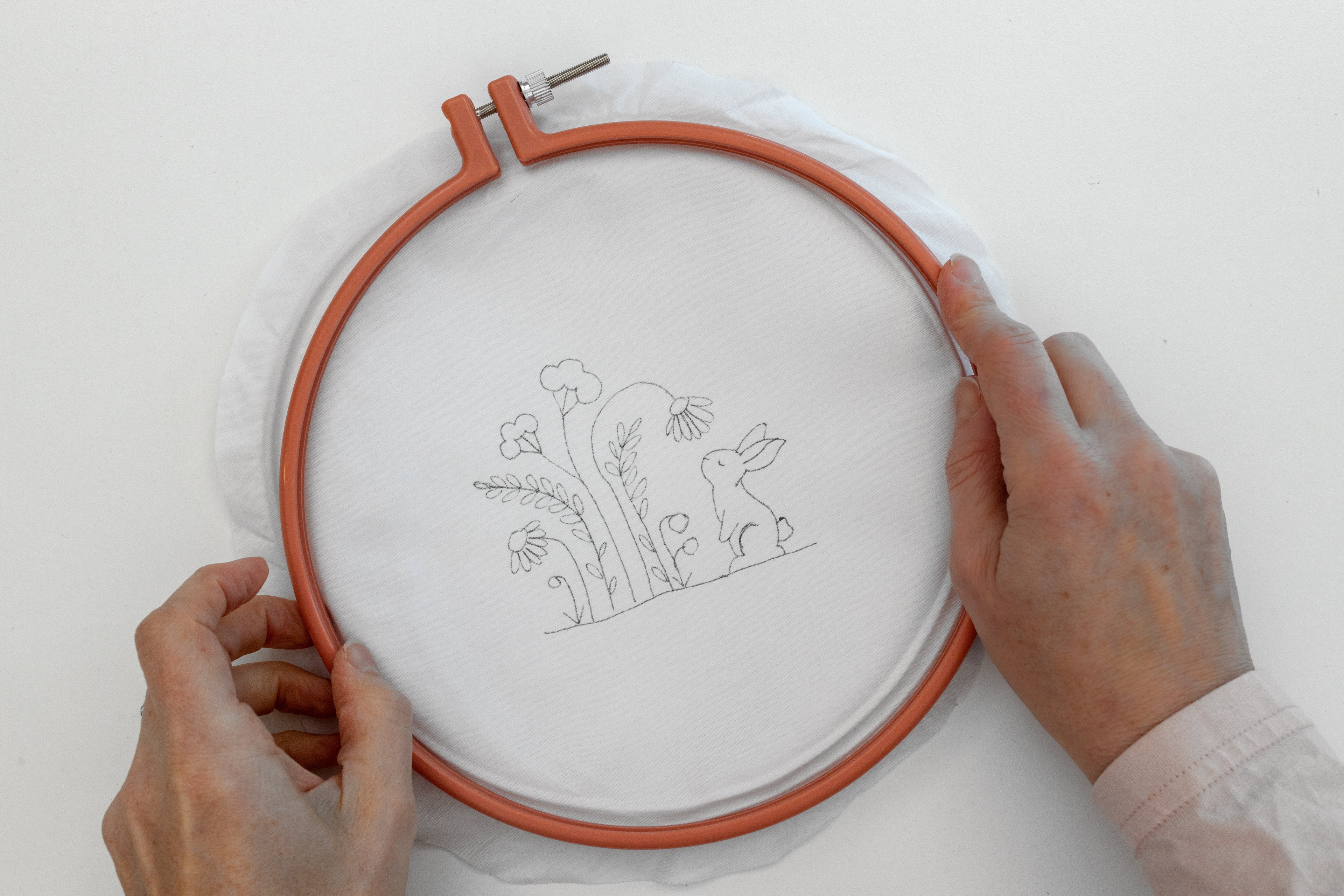 Hands press the outer hoop over fabric with the Bunny Blooms pattern drawn on.