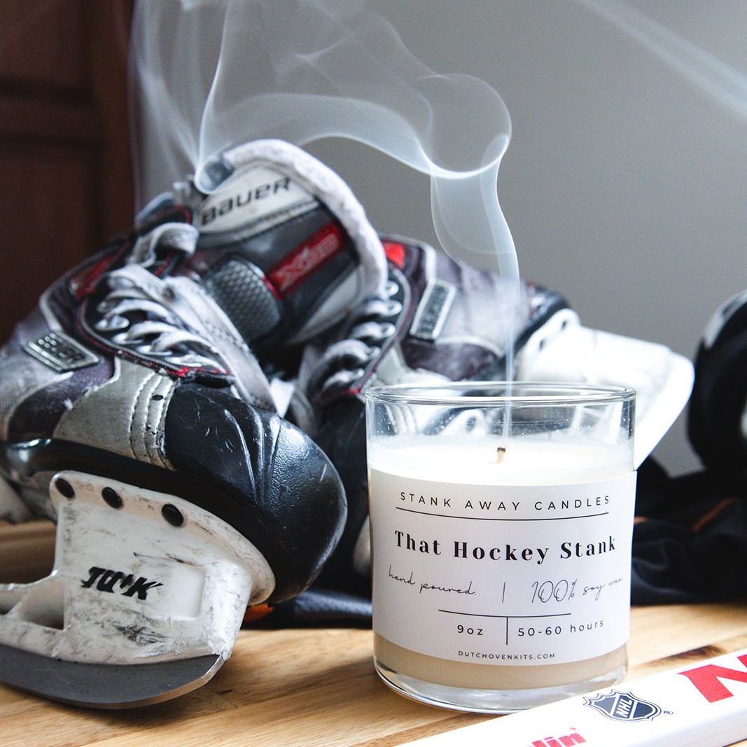 A white hockey candle sits on a wood table with a pair of ice hockey skates and a hockey stick. That hockey stank.