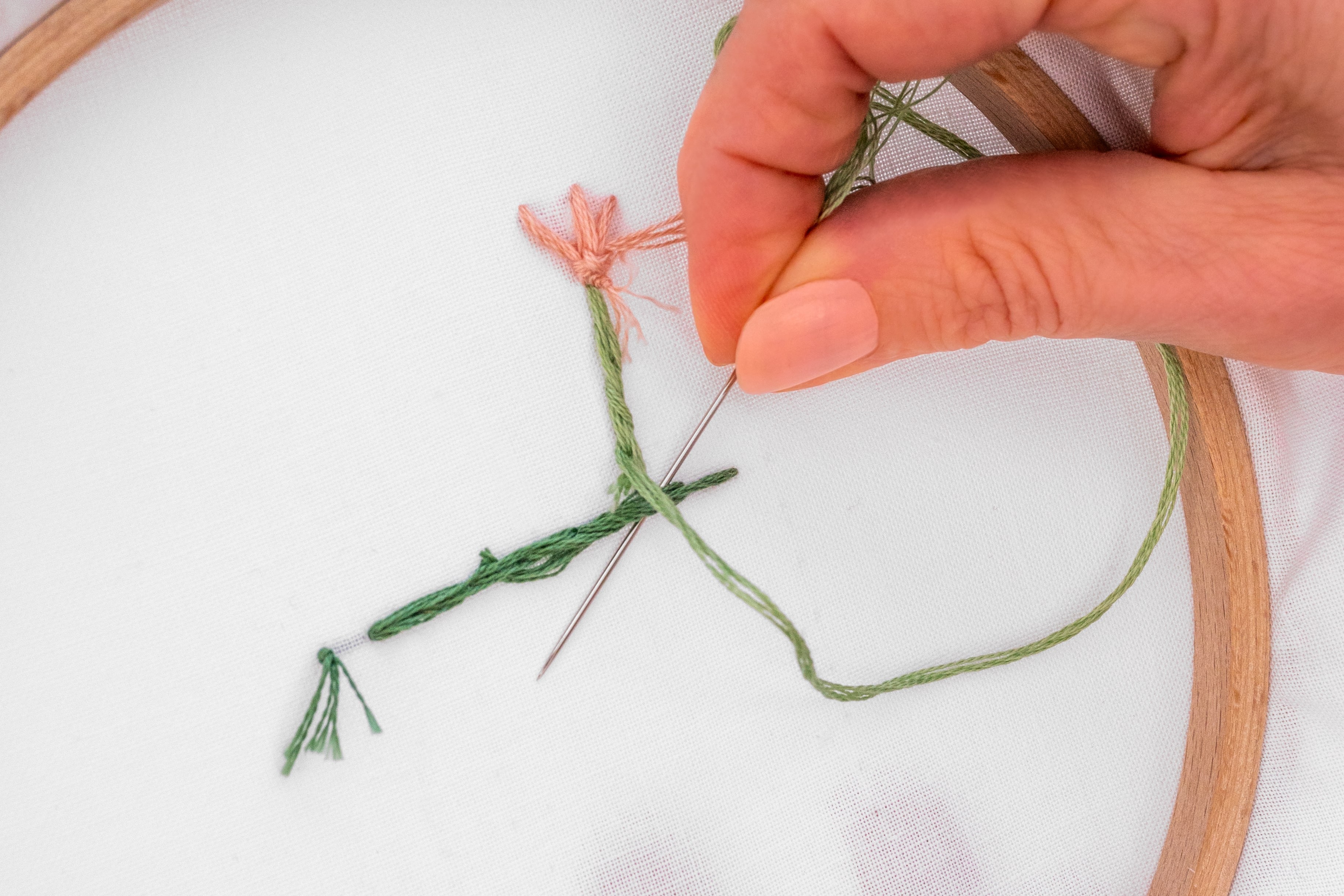 A hand brings a needle down through a bit of stitching.