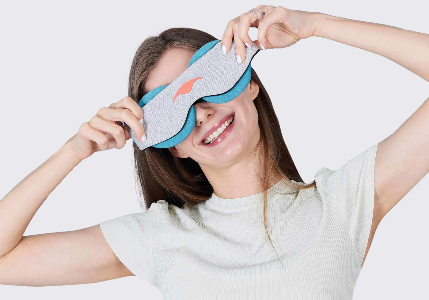 A smiling girl holding an eye mask with light blue cooling eye cups against her face.