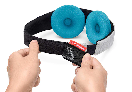 A hand pinching one of 2 blue eye cups attached to the black head strap of a cooling sleep mask with beads.