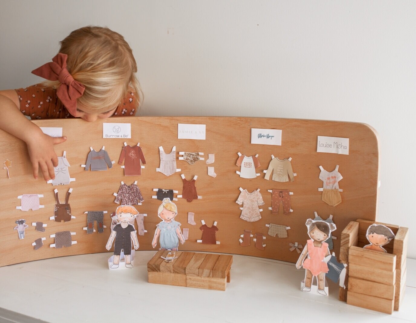 A little girl looks at her dressing station with paper clothes hung up and paper dolls.