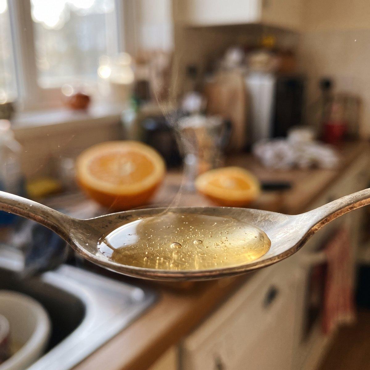 A spoonful of pale golden liposomal liquid with tiny bubbles in a sunny kitchen
