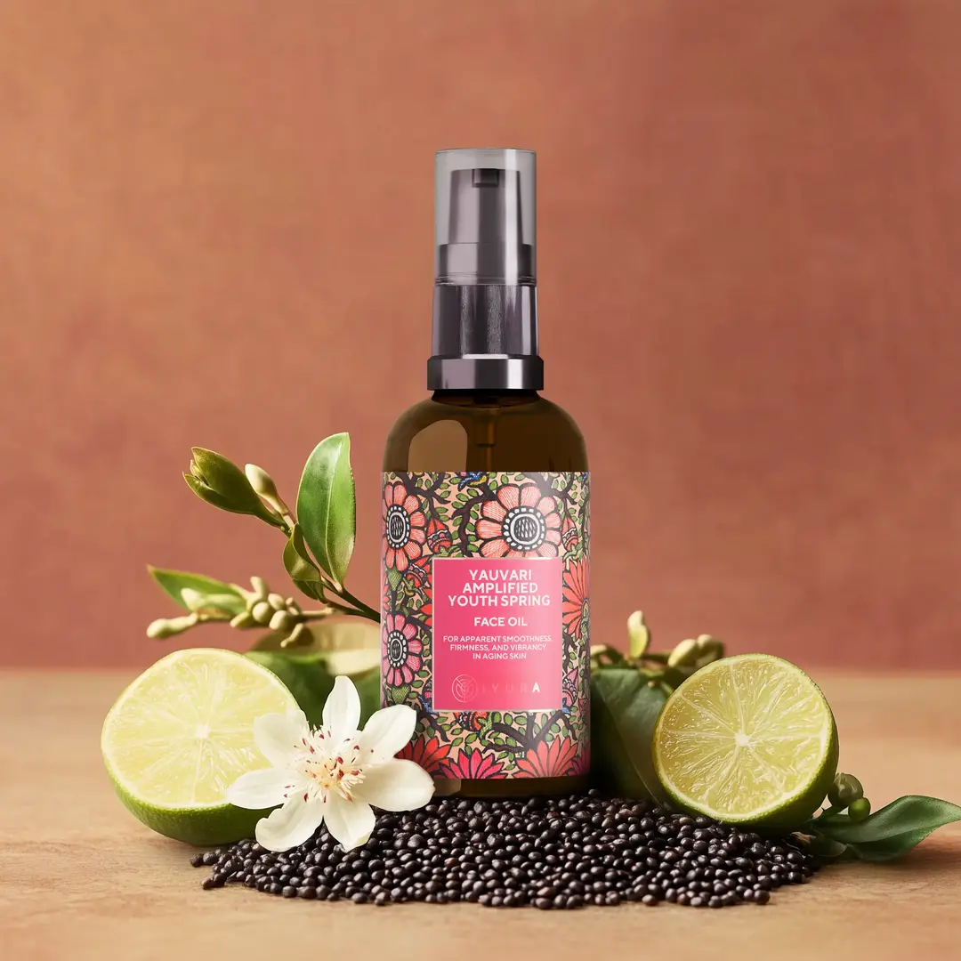 A bottle of Yauvari amplified youth spring surrounded by ingredients like black gram, cut in half limes, neroli flowers with it's buds and leaves.