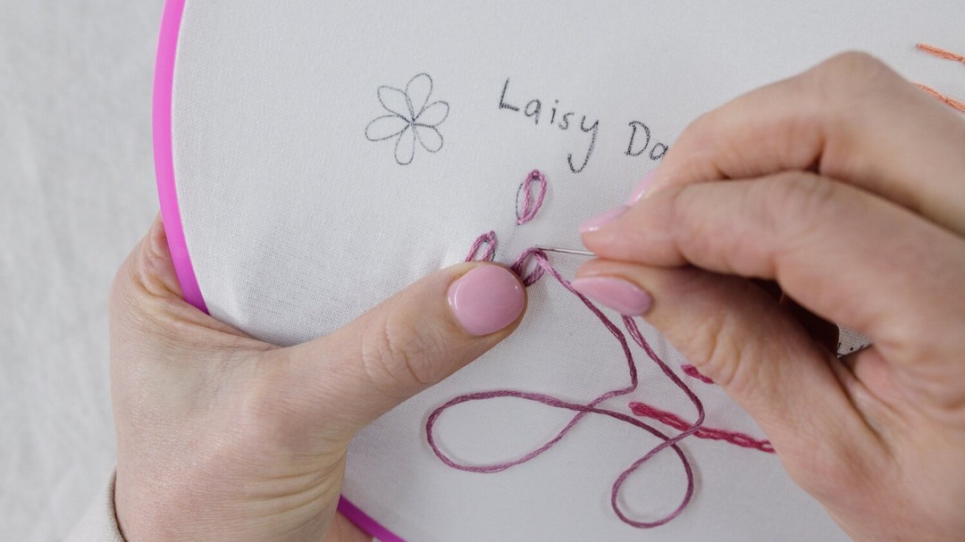 This image shows Step 4 of lazy daisy, doing a little stitch over the end of the loop.