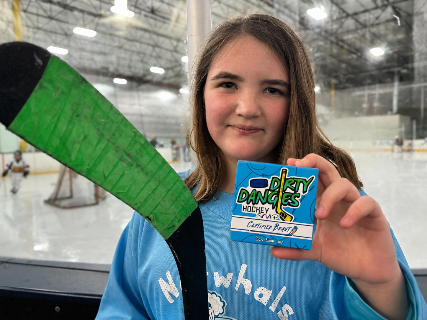 female youth hockey player in an ice rink holding a certified beaut lavender lemongrass hockey soap bar and a hockey stick.
