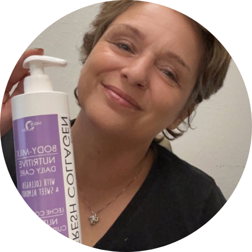 older woman smiling at the camera and holding up a bottle of Noche's Fresh Collagen Body Milk