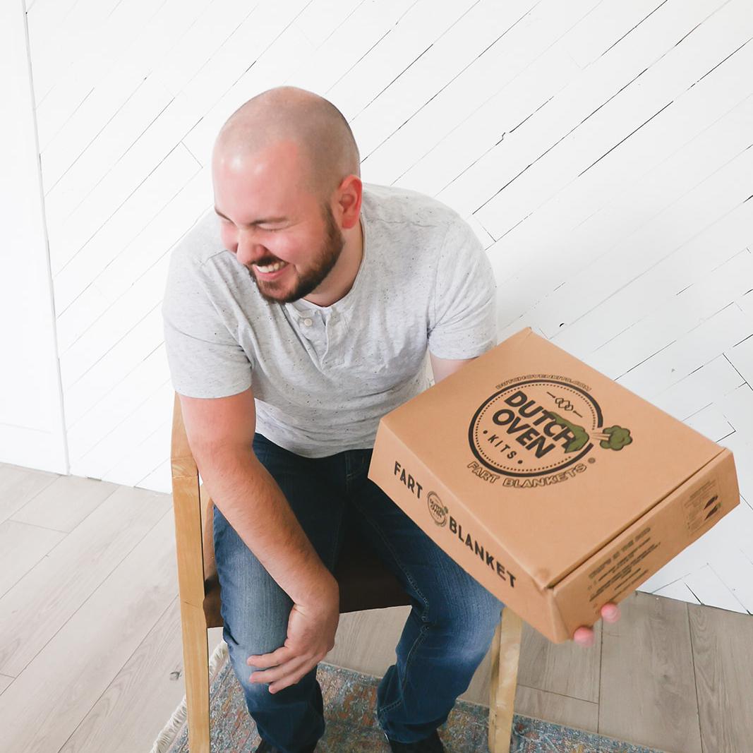 A man opening a green dutch oven kits gift box and laughing