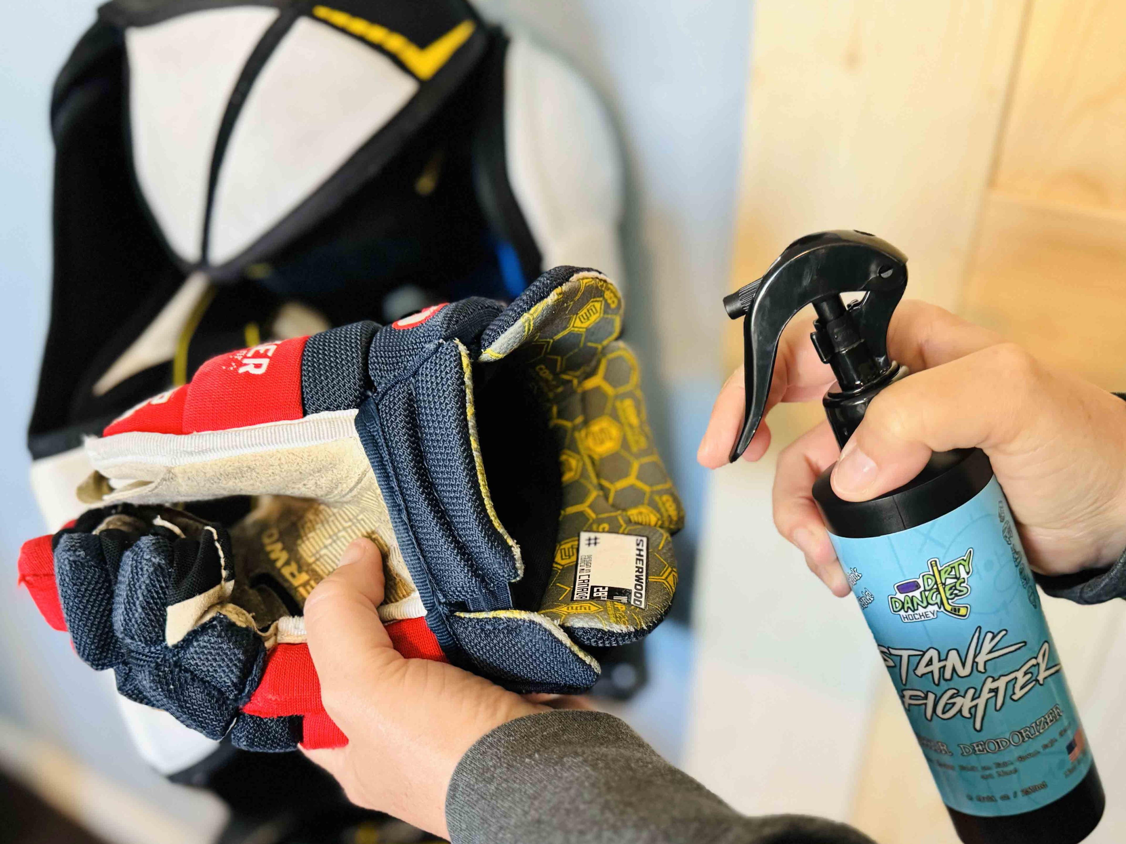 A woman spraying a hockey glove with stank fighter deodorizing hockey spray