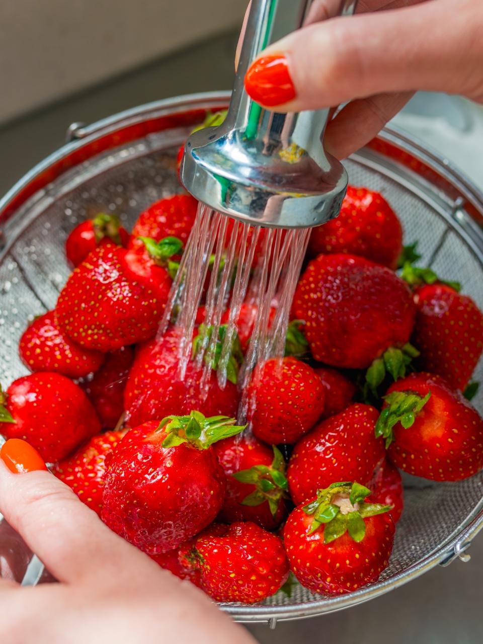 Close-up of hands rinsing fresh strawberries under running water