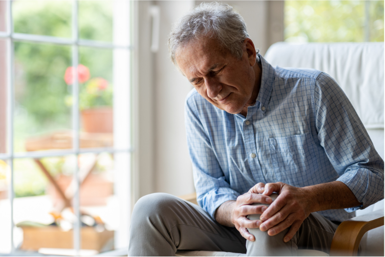 Man clutching knee in pain sitting on his couch