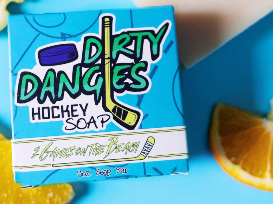 A yellow 2 games on the beach hockey soap bar on a blue background with a blue box, lemons and lavender