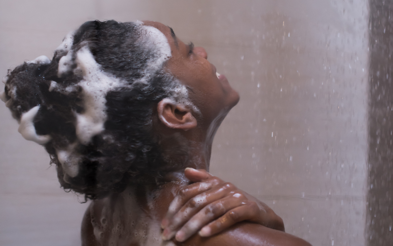 black woman washing her hair with shampoo in the shower to prevent dry hair
