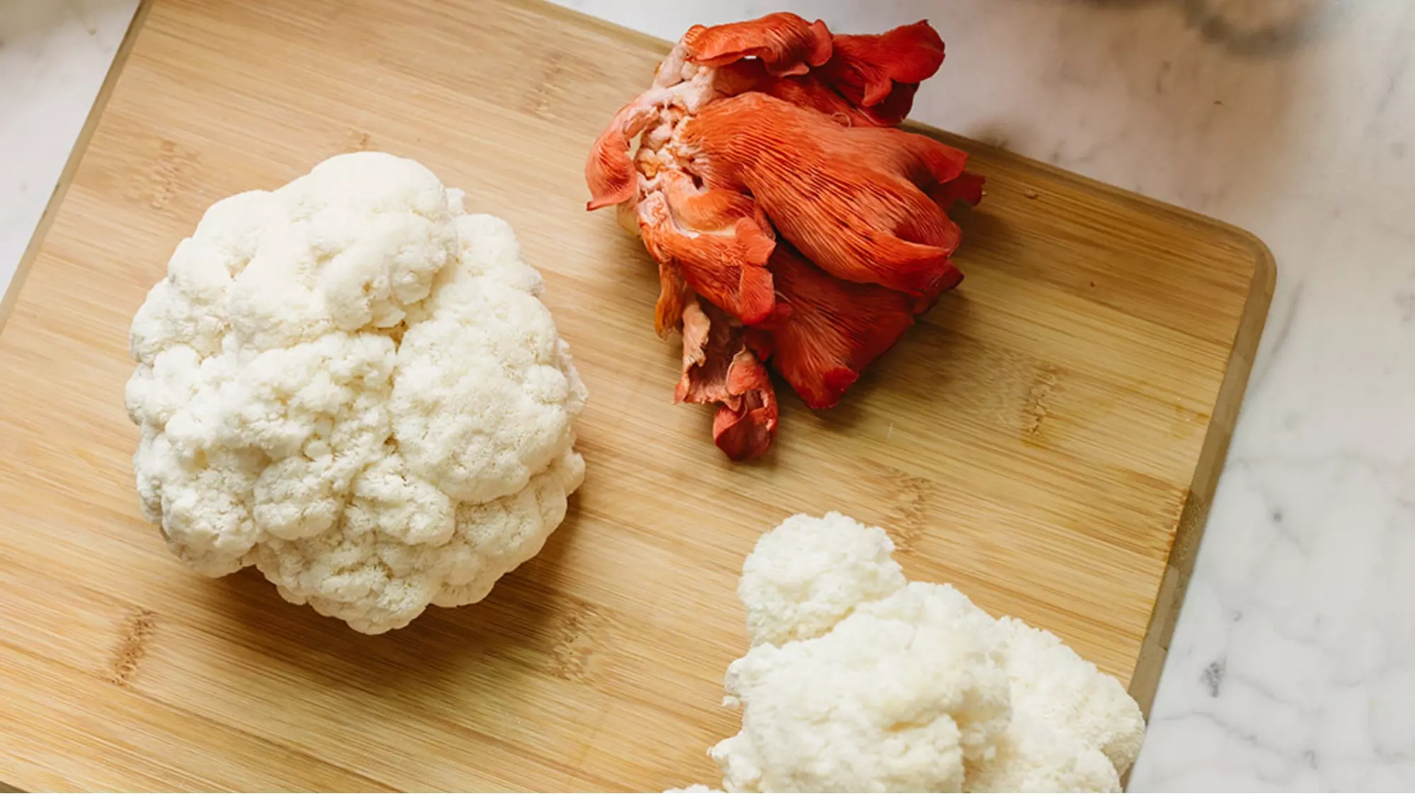 Mushroom growing harvest featuring fresh white lion's mane and red oyster mushrooms on bamboo cutting board, showcasing homegrown edible mushroom varieties ready for cooking and culinary use
