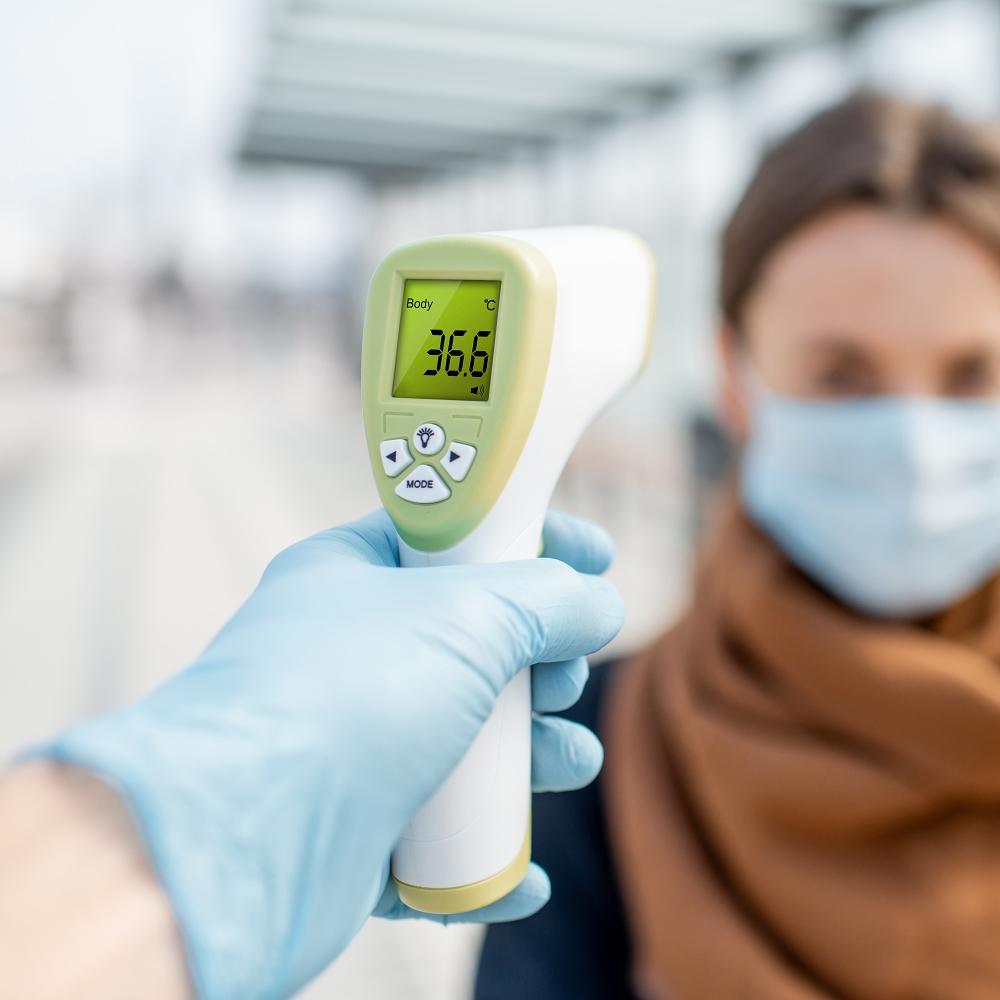 Measuring temperature of a young woman in face mask at a checkpoint outdoors