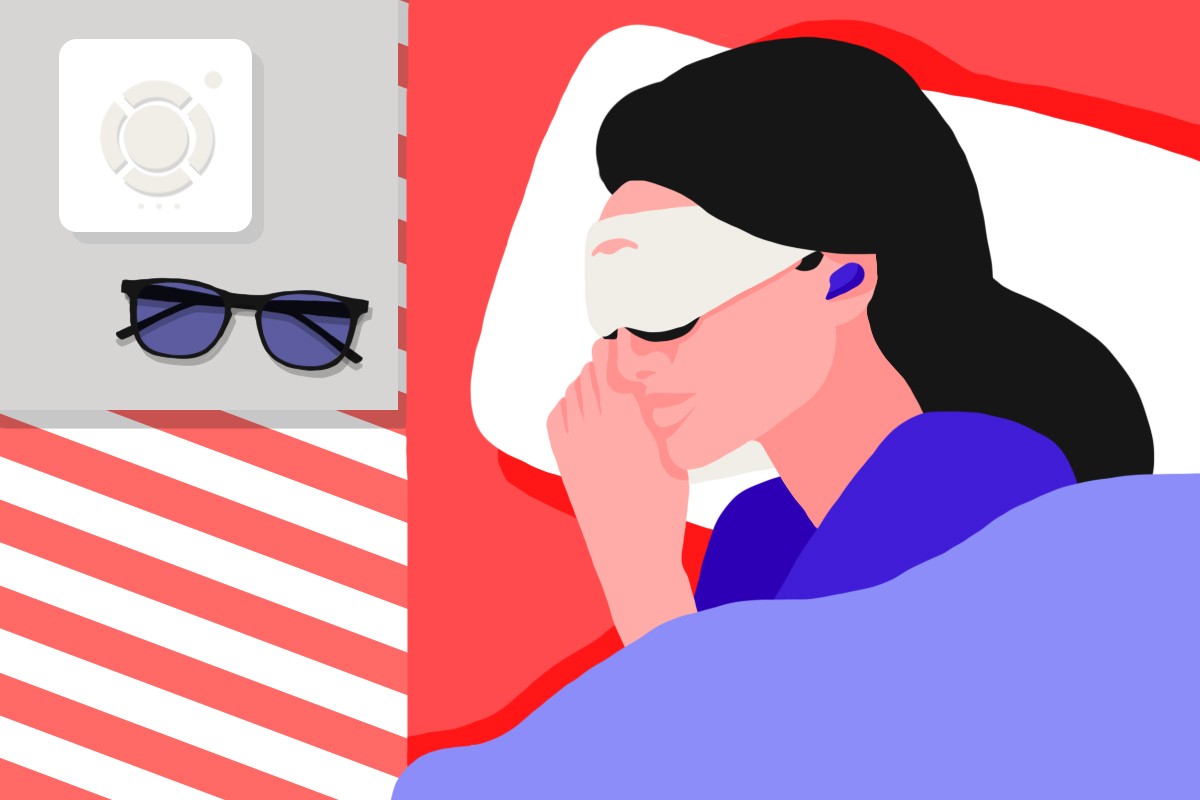 A female night shift worker lying in bed wearing a sleep mask and earplugs. Beside her on a table are the best products for night shift workers: a white noise machine and a pair of blue light blocking glasses.