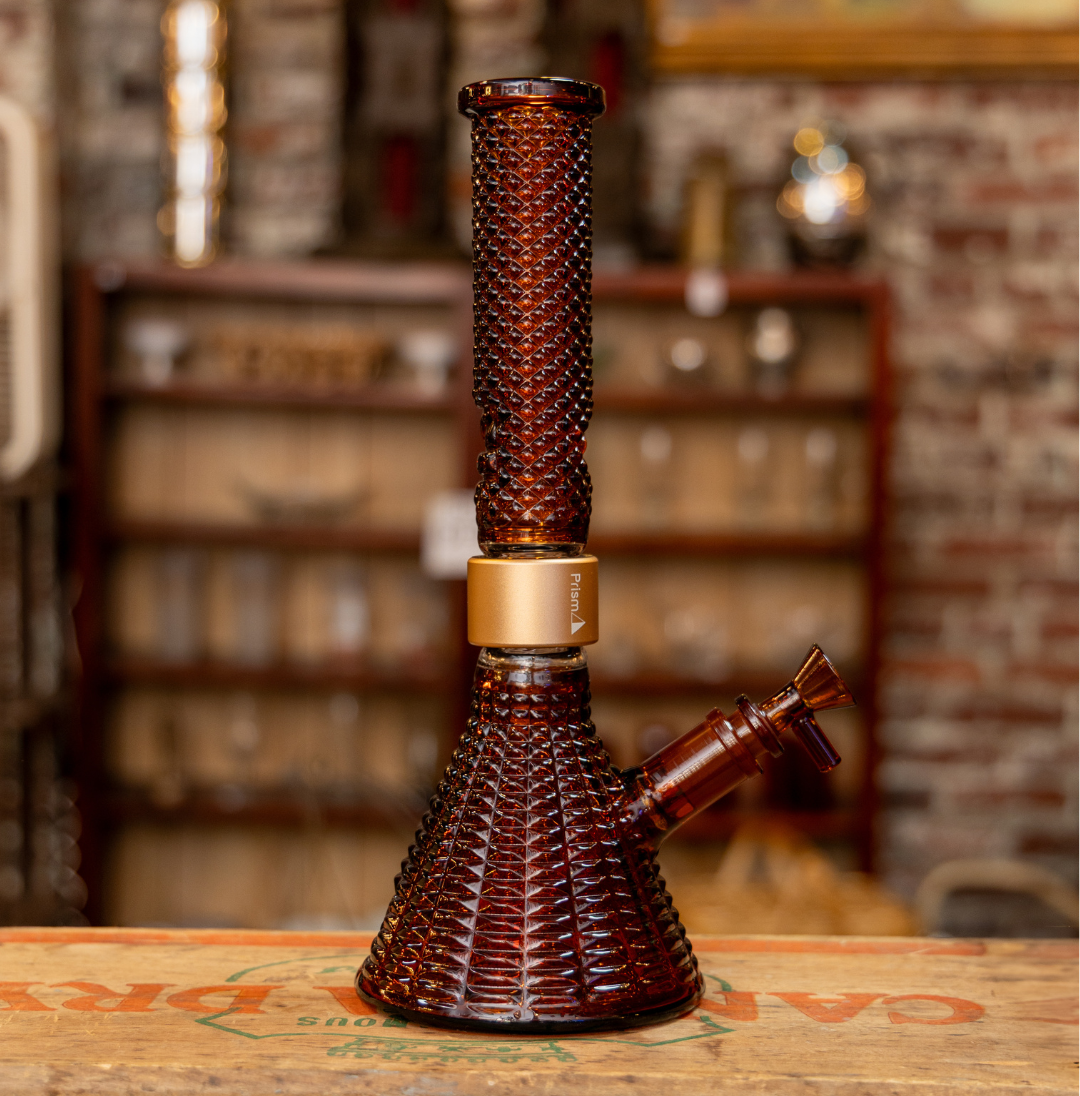 The Jane West x Prism MINI Amber Beaker bong displayed as a home decor centerpiece in a mid-century modern living room, illustrating how premium amber borosilicate glass integrates into stylish, contemporary interior design.