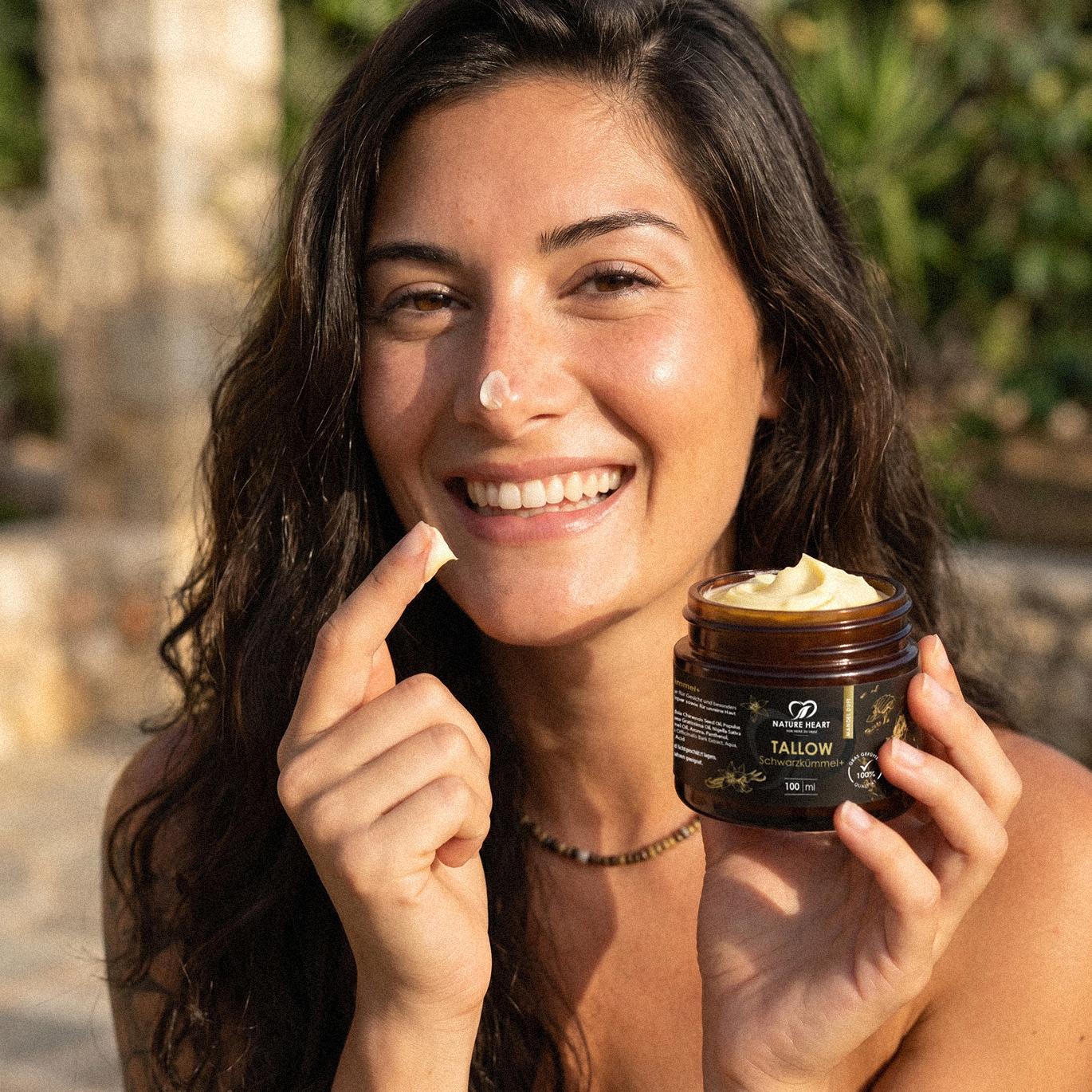 Lachende Frau mit Tallow-Klecks auf der Nase präsentiert Nature Heart Tallow Schwarzkümmel+ Pflegetiegel im Sommer