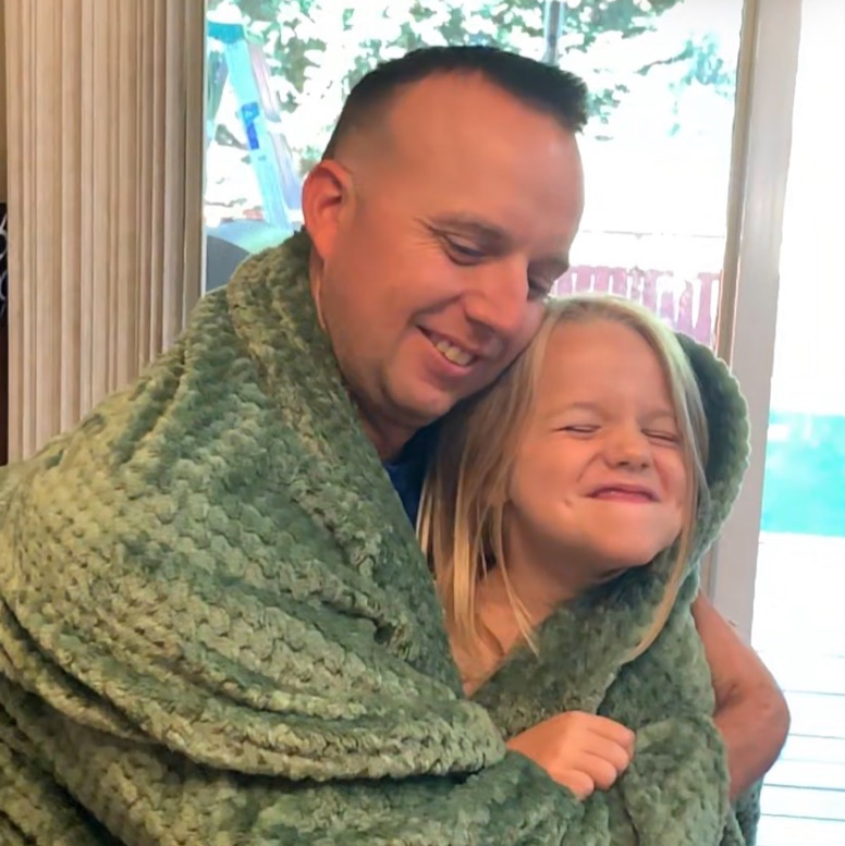 A man and his daughter smiling while snuggling under a green dutch oven kits blanket
